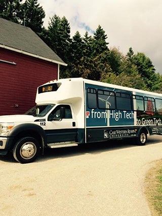 Shuttle Bus for Case Western Reserve University with text from High Tech to Green Tech written on side, parked in front of red barn with tall trees in background