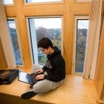 Student works on a laptop in front of a window overlooking campus
