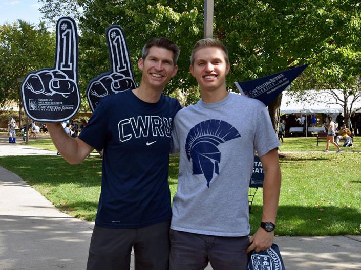 A CWRU student with his dad holding up foam fingers with the school logo on them