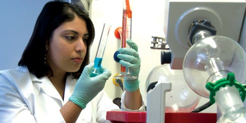 Female researcher in white lab coat working with multiple test tubes, with research equipment in foreground