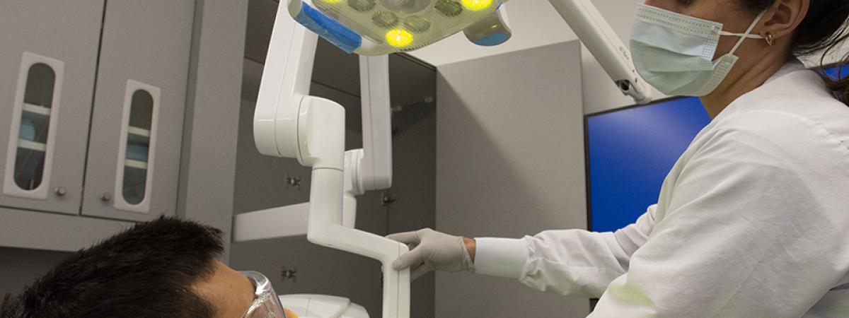 A woman with a mask on adjusts an x-ray next to a man's face 