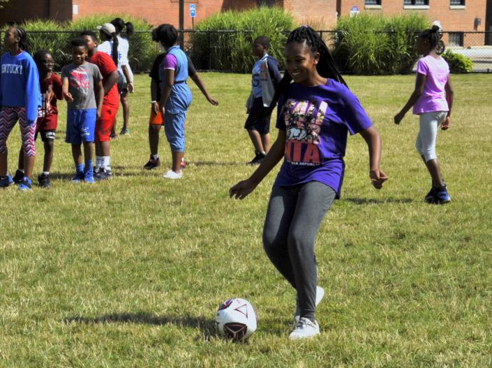 Girl playing soccer with group of students behind her