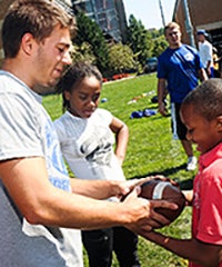 CWRU student playing football with two young people on campus, with students in the background
