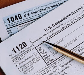 1120 US corporation income and 1040 US individual income tax forms overlaid on each other, with gold pen on top