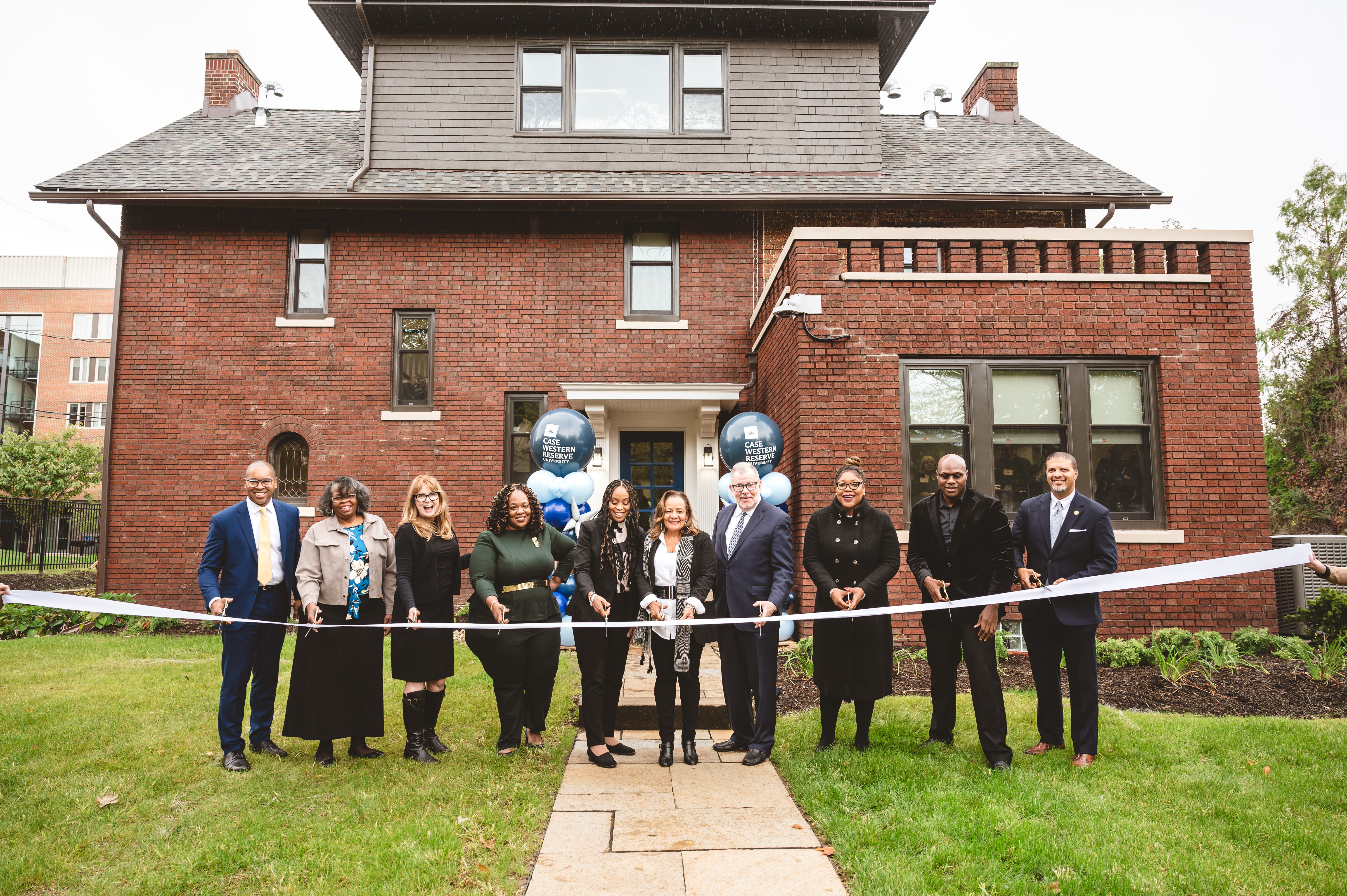 A row of people cutting a ribbon in front of a house