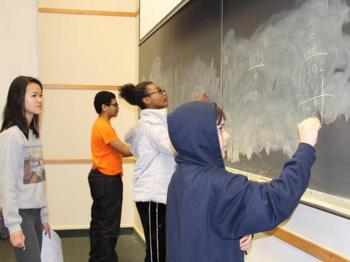 4 students at a chalkboard solving math problems
