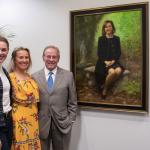 Kate Shaughnessy Biggar, Anne Shaughnessy Marchetto and Michael Shaughnessy stand next to a portrait of Marian Shaughnessy hanging on a wall