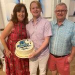Three people standing together, one person is holding a cake that says Congrats Charlie