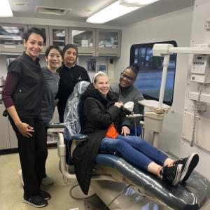 Four people from CWRU School of Dental Medicine pose with a happy patient in the dentist chair
