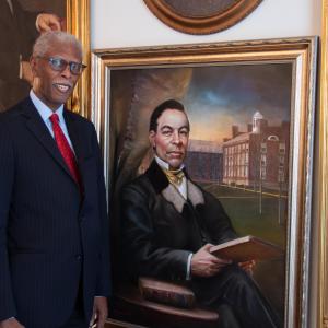 David A.G. Johnson Jr. stands beside a portrait of John Sykes Fayette while wearing formal attire
