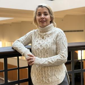 Nima Firouzi stands next to a railing in an indoor setting while wearing a turtleneck sweater