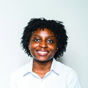 Nia Badley smiles at camera in front of a plain portrait backdrop while wearing formal attire