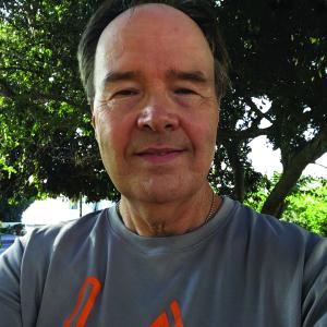 Ray Billig smiles at camera in an outdoor setting in front of a tree while wearing casual attire