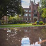 A student walks through the Mather Quad on CWRU campus, their reflection in the fountain