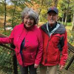 Marie and Chuck Grossman smile at the camera, both wearing cool-weather clothing, in front of an outdoor railing at a Cleveland Metropark