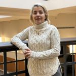 Nima Firouzi stands next to a railing in an indoor setting while wearing a turtleneck sweater