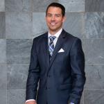 Tyler Miller stands behind CWRU-branded chair and in front of a gray marble tile wall while wearing formal attire and smiling at the camera