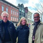 From left: David and Gayle Noble and Dean Dexter Voisin smile at camera while wearing cool-weather jackets in front of a commercial space.