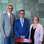 From left: Robert Kowal, William Grissom and Adele Suttle standing in front of a marble stone wall while wearing formal attire behind a CWRU-branded chair