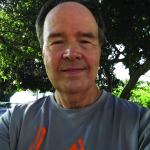 Ray Billig smiles at camera in an outdoor setting in front of a tree while wearing casual attire