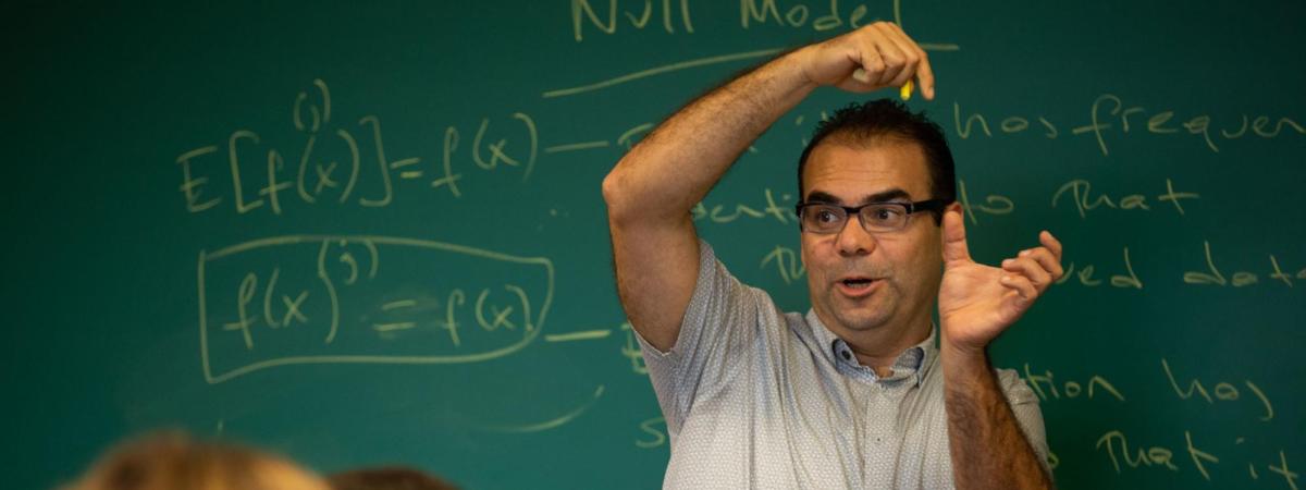 Professor standing in front of a chalk board with hands raised
