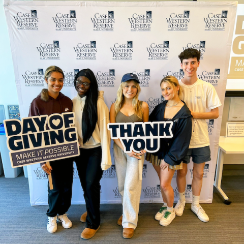 Five students stand in front of a CWRU step-and-repeat holding signs saying "Day of Giving" and "Thank you!"