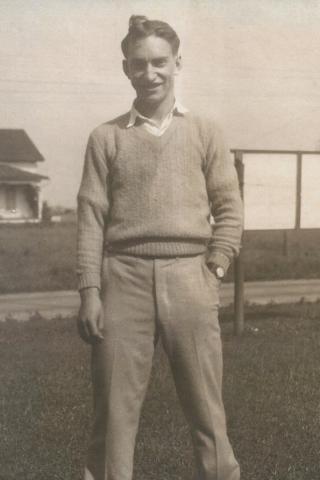 A sepia image of a young Jack Green standing outside, wearing a sweater and collared shirt