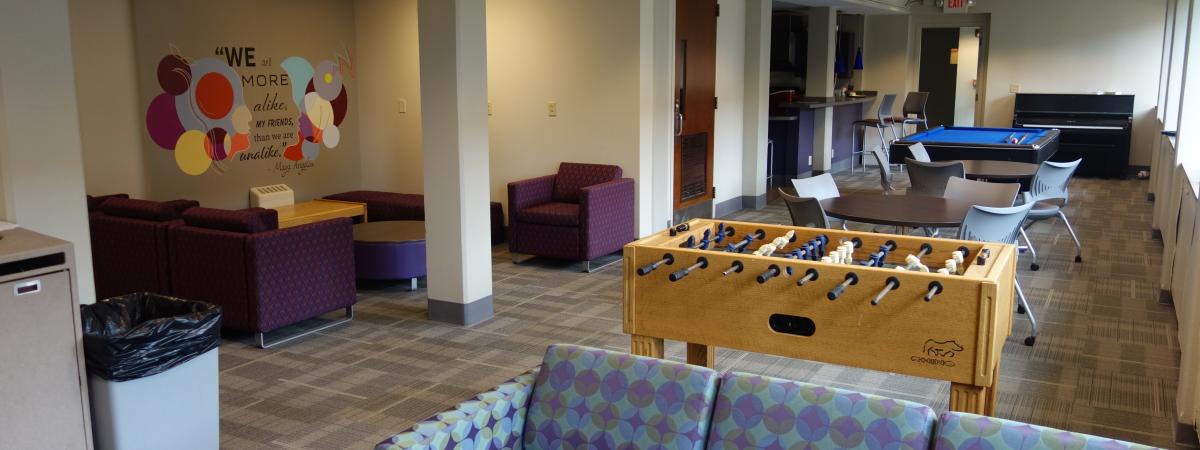 Alumni House common room with furniture, game tables, and mural
