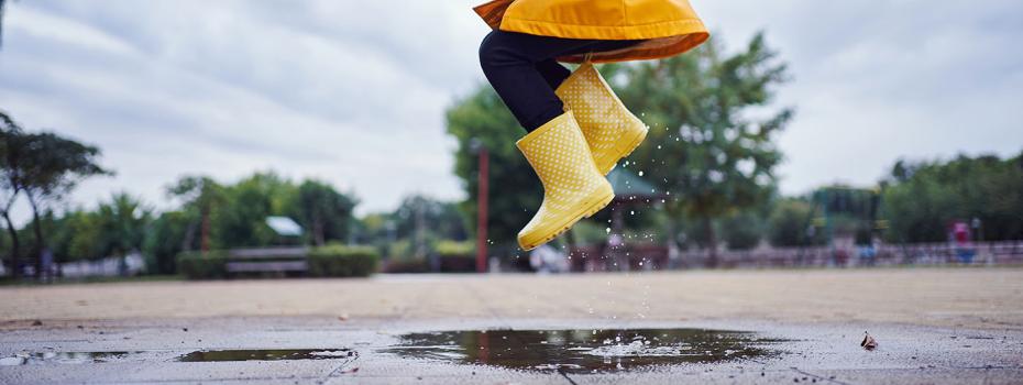 Child in yellow raincoat jumping in a puddle