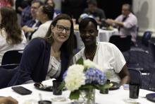 Two employees sitting at a table and smiling with blue and white flowers in the middle