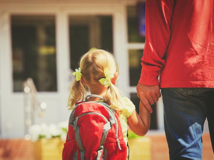Child with backpack holding the hand of an adult