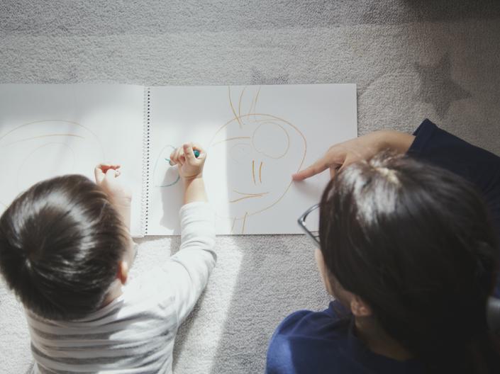 Child and adult on the floor drawing a picture