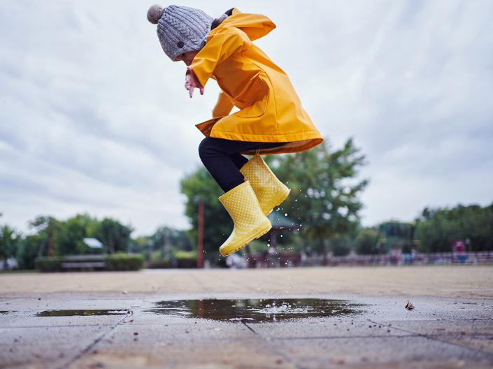 Child in yellow raincoat jumping in a puddle