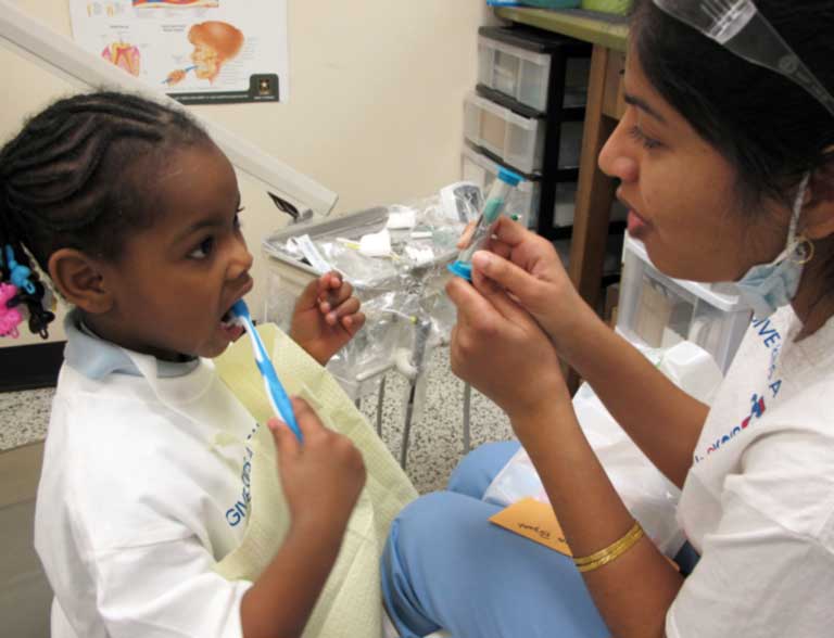 photo of a dentist teaching a child to brush her teeth