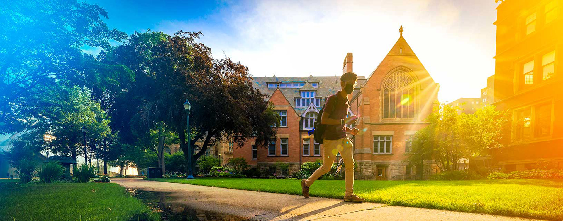 Photo of a masked student walking across campus with blue and yellow gradients