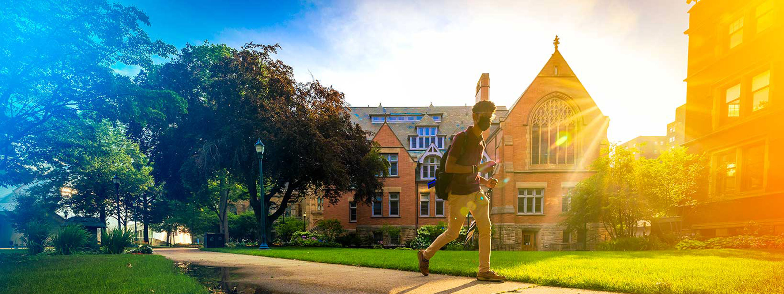 Photo of a masked student walking across campus with blue and yellow gradients