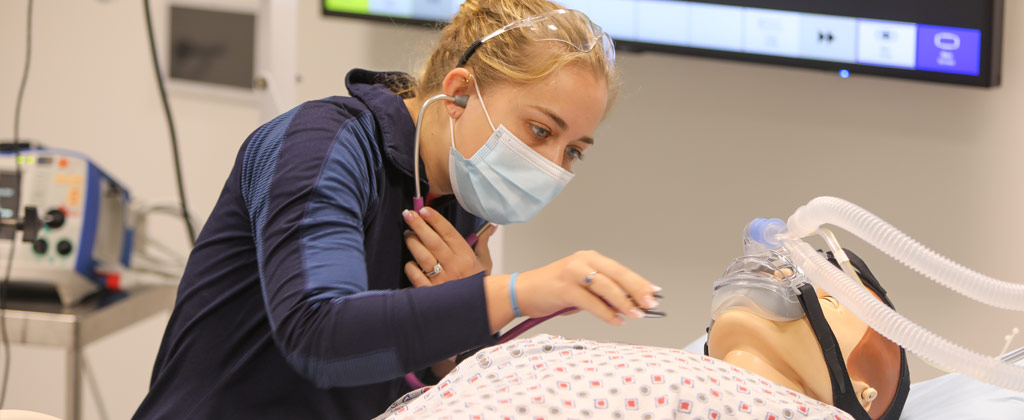 Photo of a nursing student using a stethoscope on a body mannequin