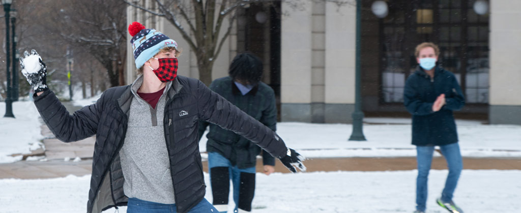 Photo of a CWRU student throwing a snowball in front of Kelvin Smith Library