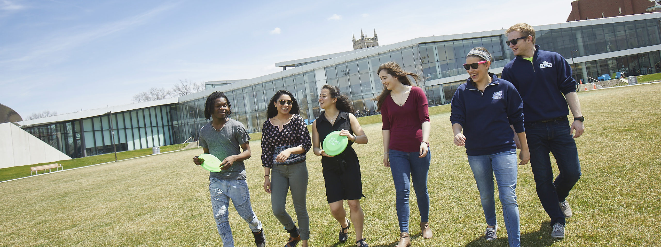 Photo of six smiling students walking across a green space with Tinkham Veale University Center behind them