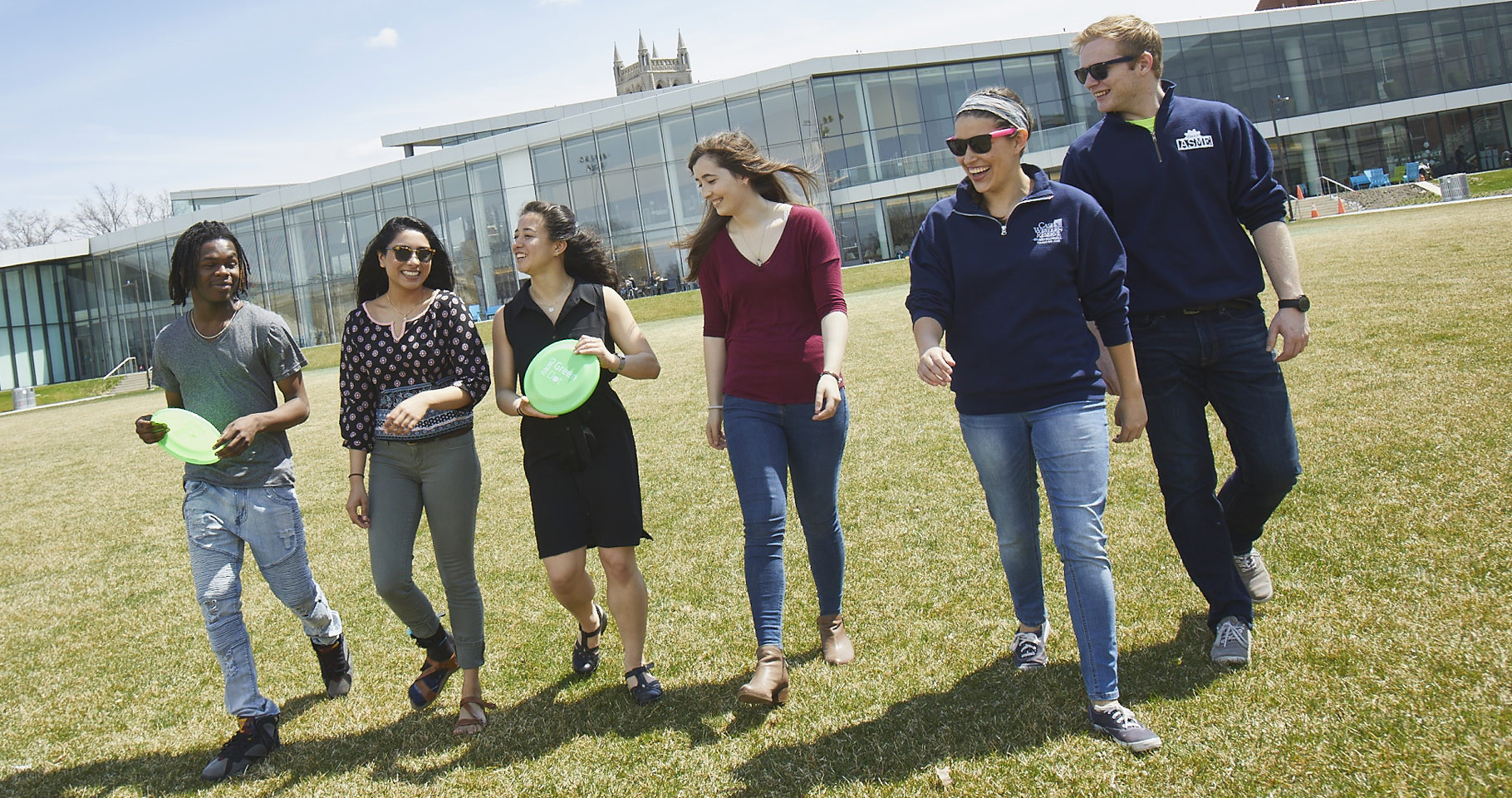 Photo of six smiling students walking across a green space with Tinkham Veale University Center behind them