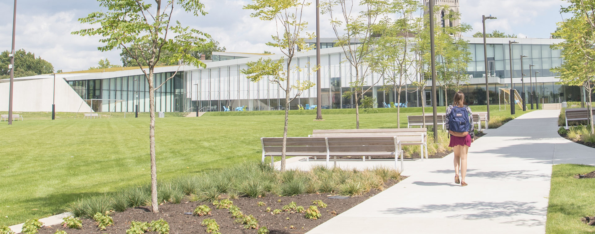 Photo from behind of a student walking down a path toward Tinkham Veale University Center on a bright clear day