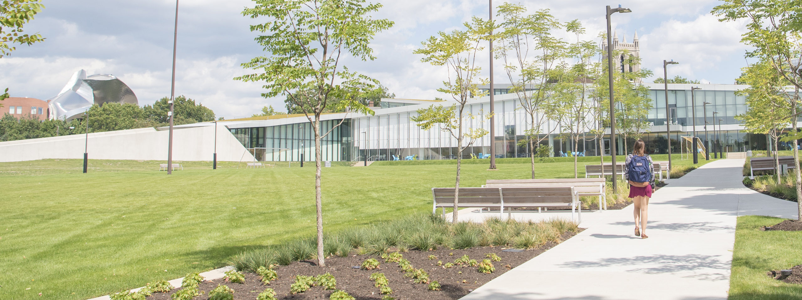Photo from behind of a student walking down a path toward Tinkham Veale University Center on a bright clear day