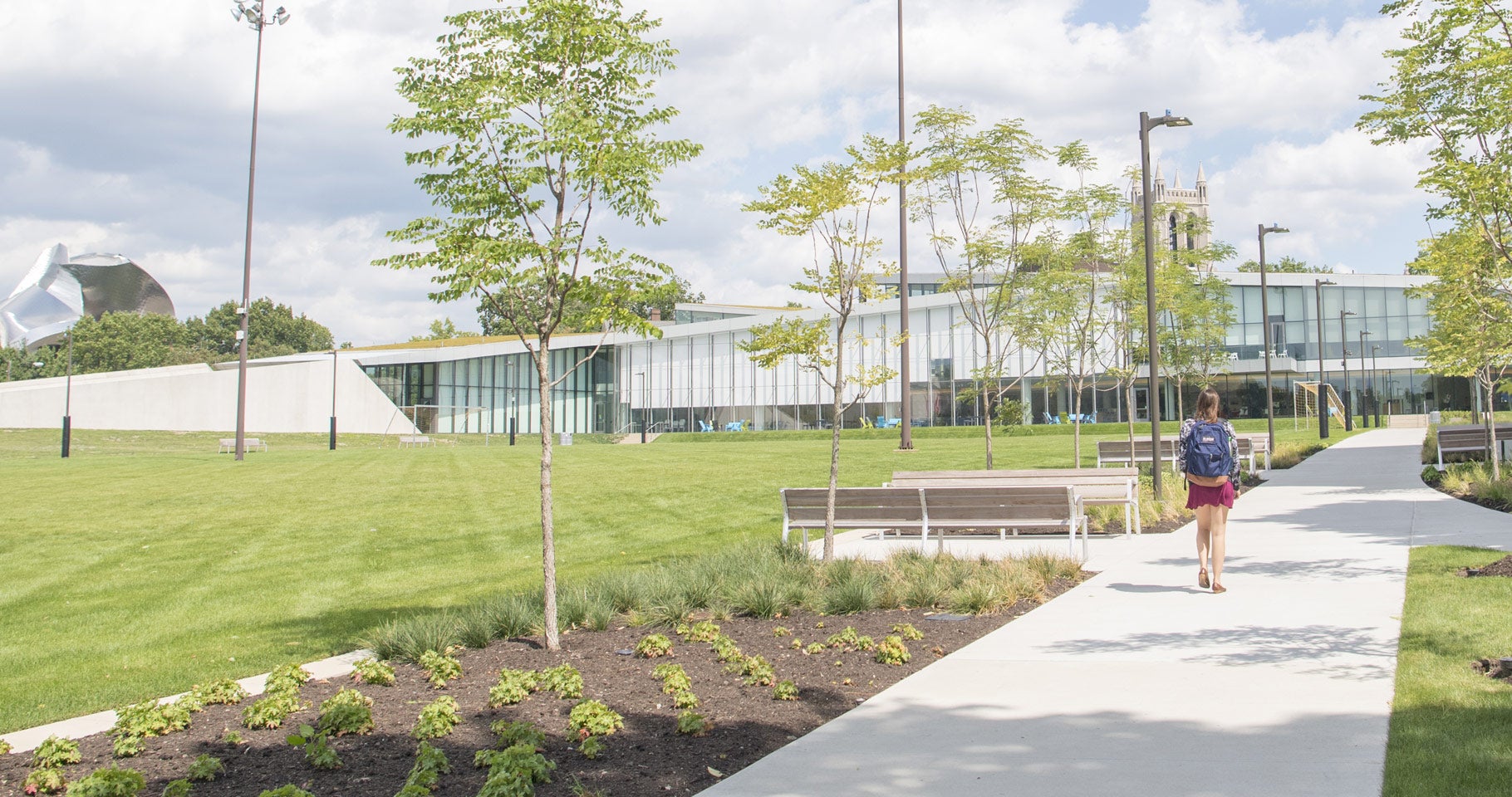 Photo from behind of a student walking down a path toward Tinkham Veale University Center on a bright clear day