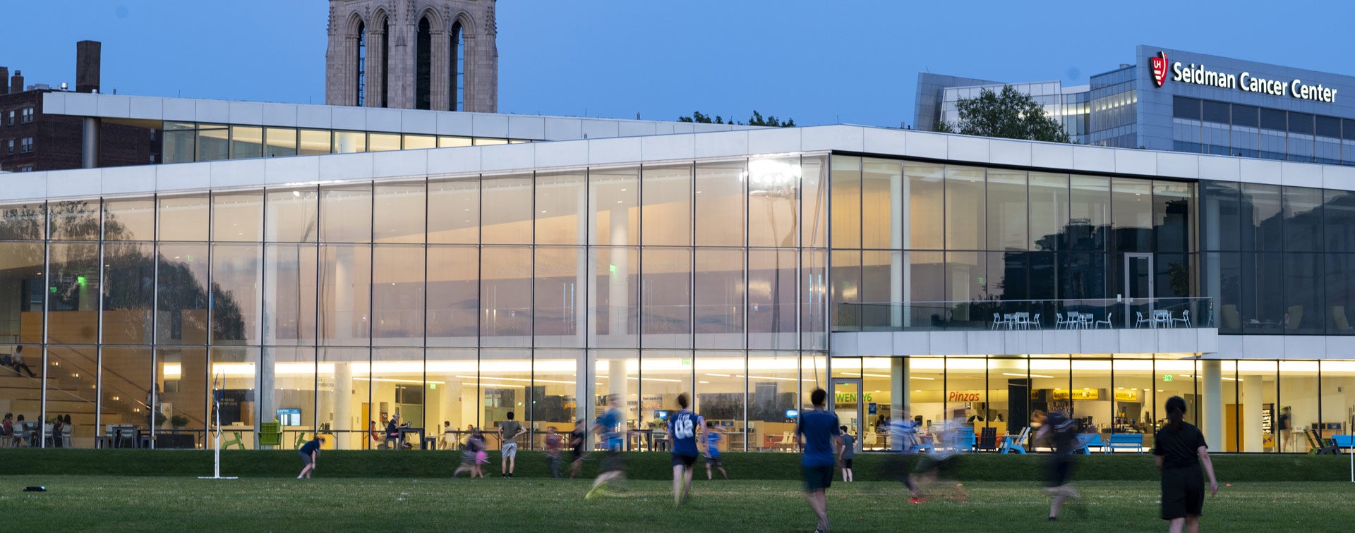 Photo of students playing a game on in the field outside Tinkham Veale University Center at dusk