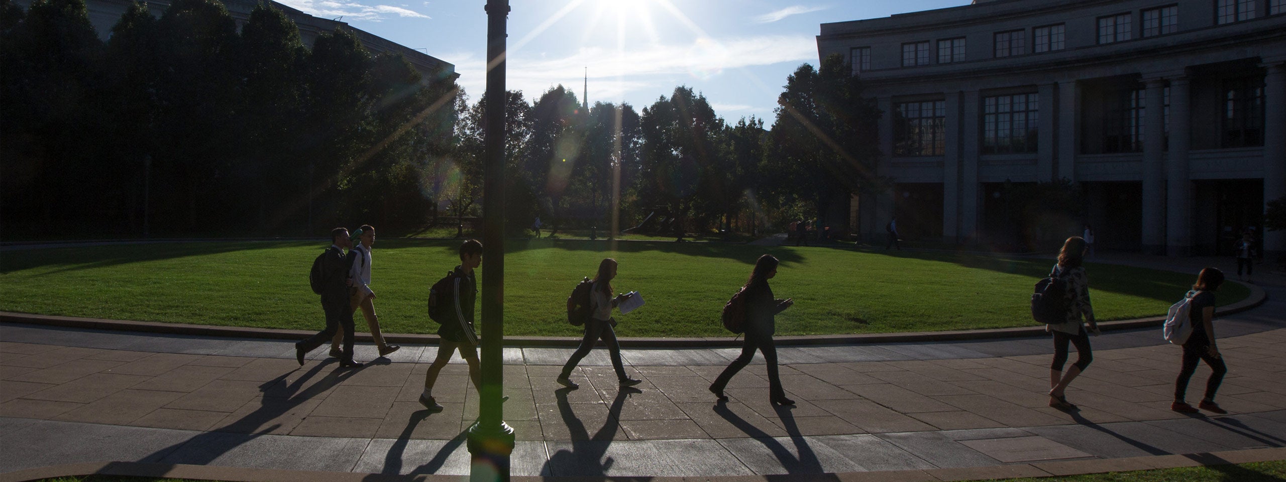 Photo of students walking at KSL Oval with the sun shining and putting a glare over the photo