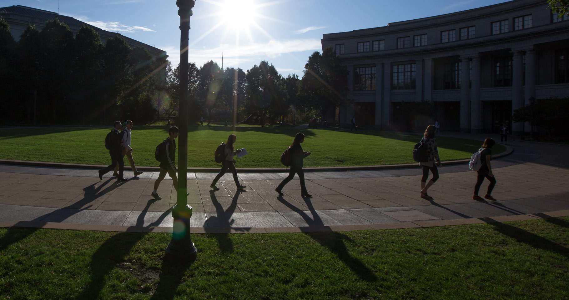 Photo of students walking at KSL Oval with the sun shining and putting a glare over the photo