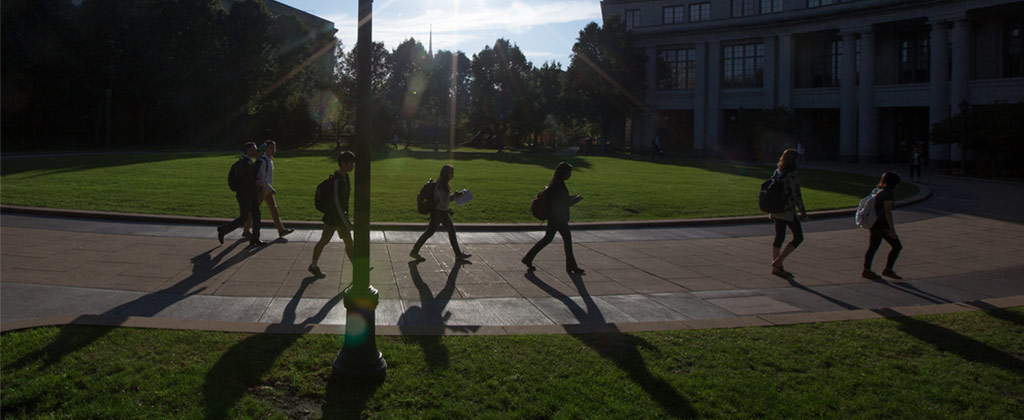 Photo of students walking at KSL Oval with the sun shining and putting a glare over the photo