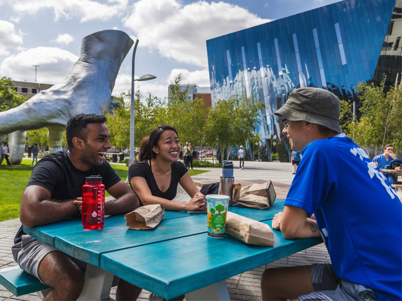 Photo of three students talking and laughing at a picnic table in the Uptown neighborhood