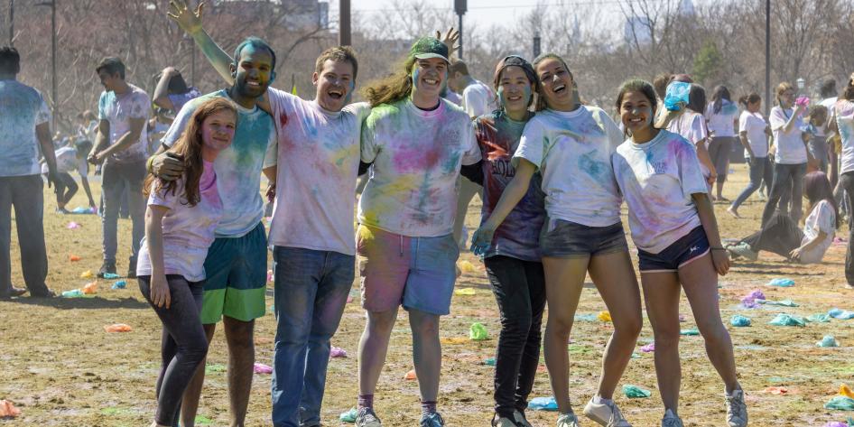 A group of students pose for a picture, covered in color, during Holi 2019