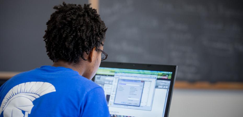 A student wearing a CWRU shirt sits facing a computer in a classroom